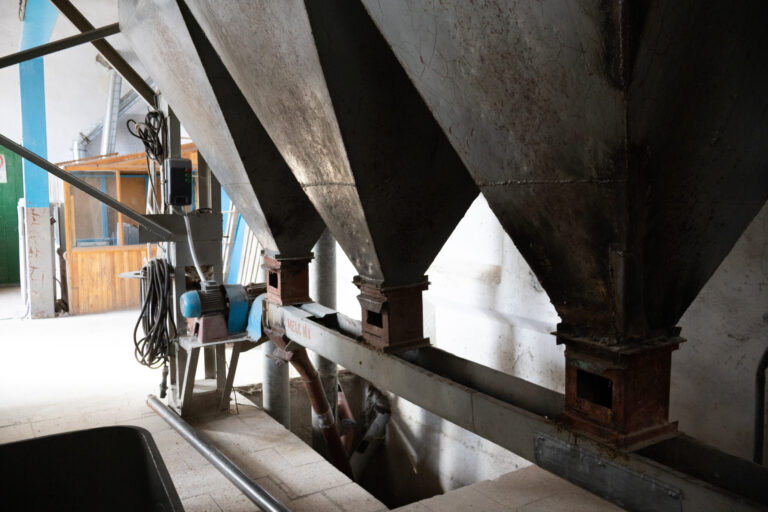 Row of heavy-duty industrial metal hoppers and funnel systems used for grain distribution and storage in a mill or factory.